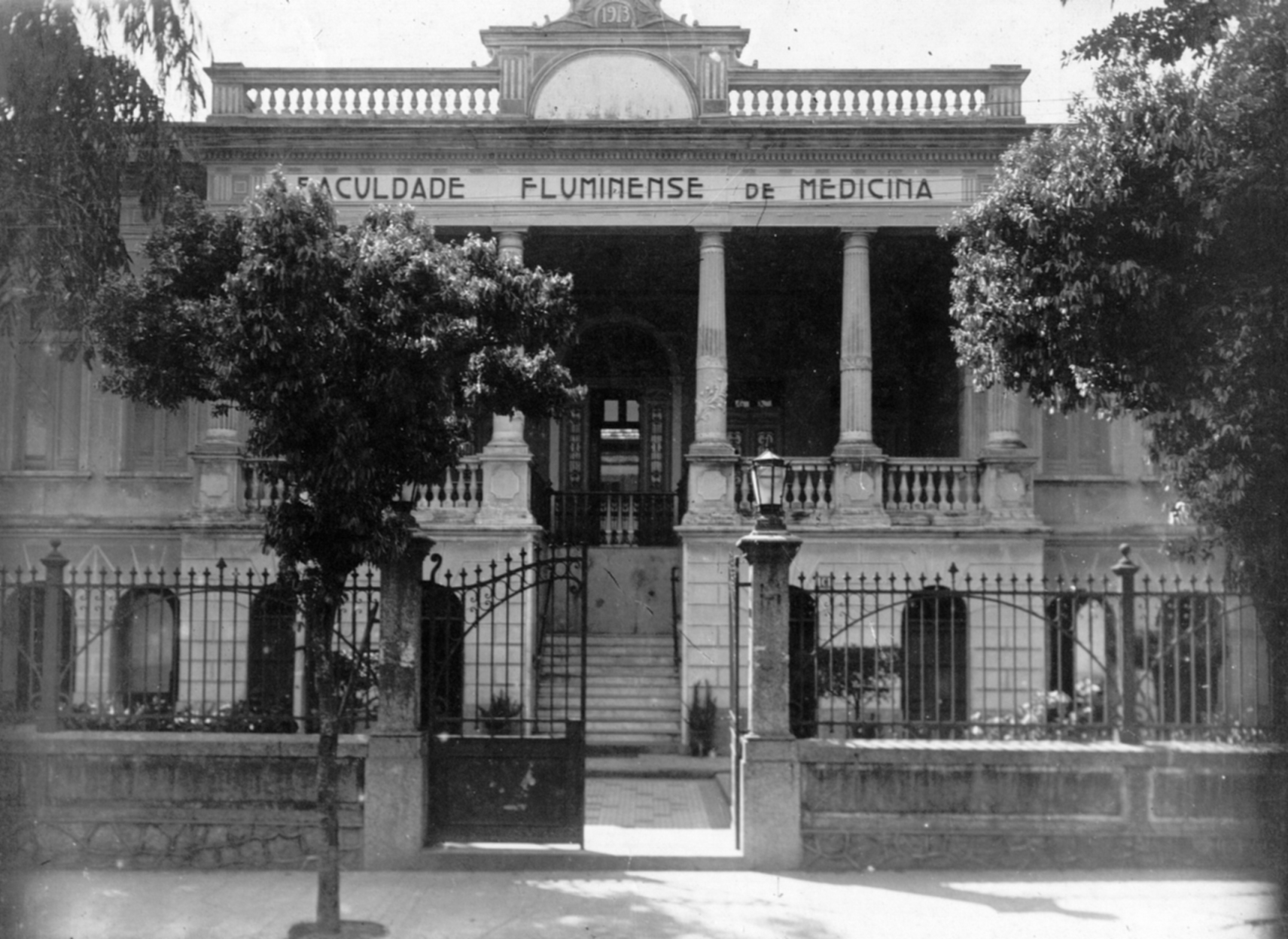 Prédio da FFM. Fachada de arquitetura eclética, entre 2 árvores na calçada o portão de entrada aberto, à Rua Visconde Moraes (atual Rua Prof. Hernani Pires de Mello). Década de [1930]